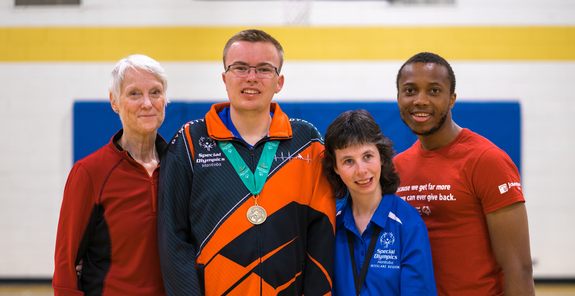 Four adults standing together smiling at the camera. All are in athletic gear. Two have medals around their necks. 