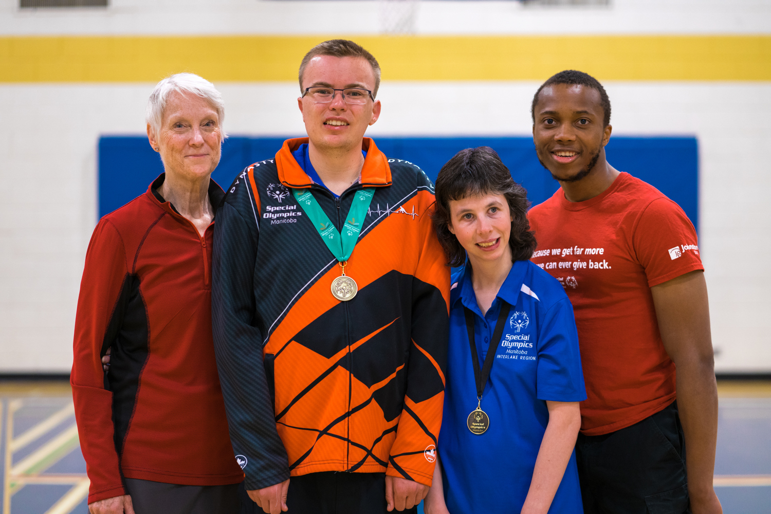 Four adults standing together smiling at the camera. All are in athletic gear. Two have medals around their necks. 