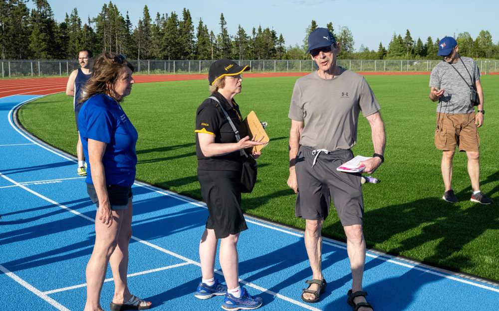 Three coaches and volunteers are standing on a bright blue track discussing amongst one another.