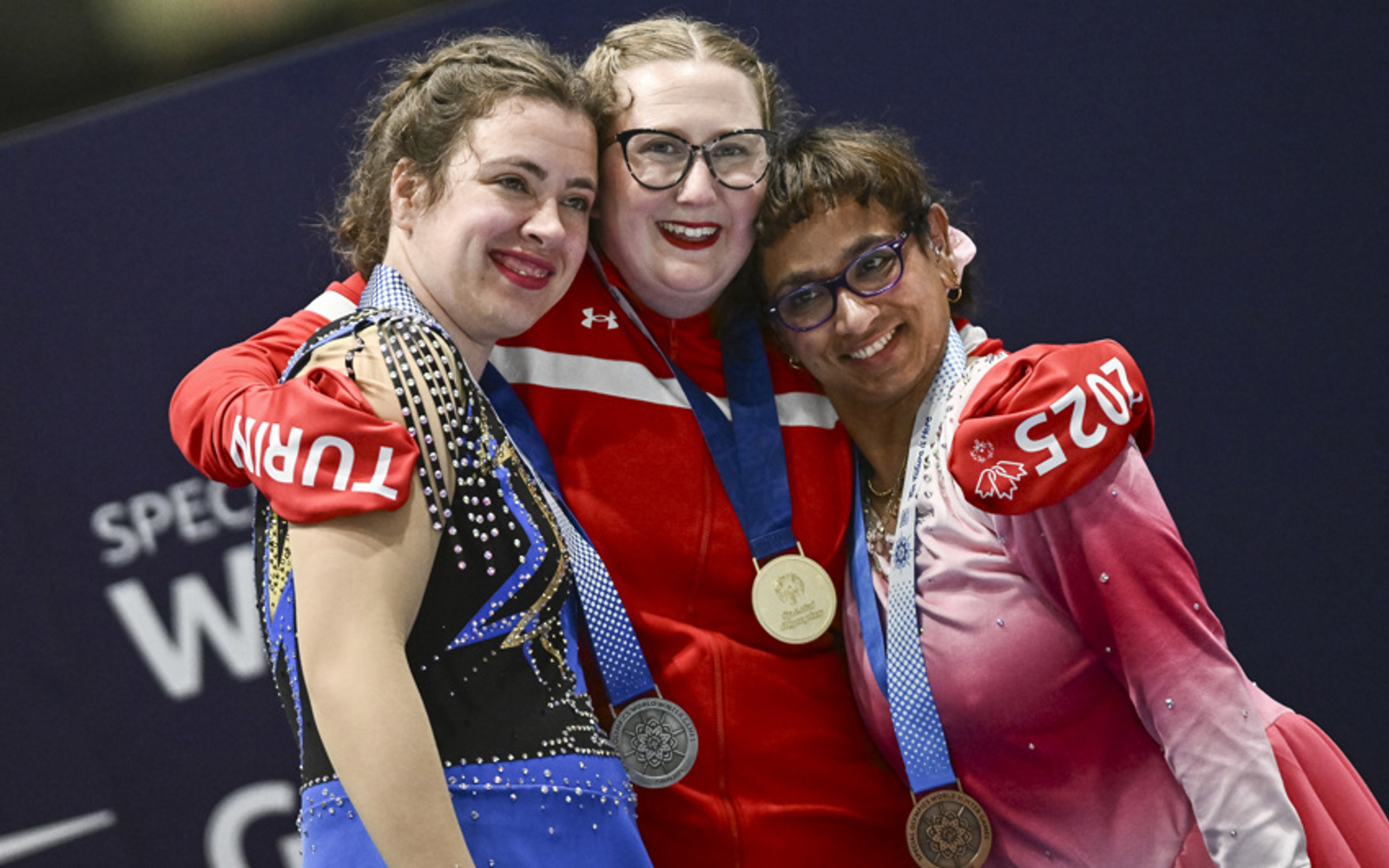 Three women in Canadian uniforms hug one another, with medals around their necks. 