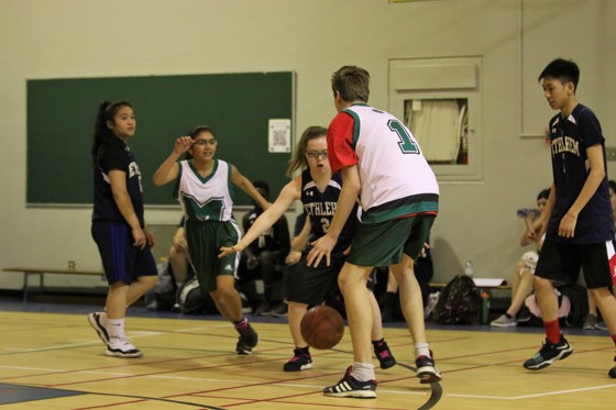 A action shot photo of a unified basketball game. Five athletes can be seen playing basketball on the court. One athlete is dribbling the ball while another is trying to defend him.