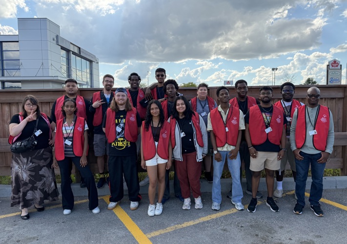 A group of 16 face to face canvassers pose together, smiling at the camera. The are all wearing red Special Olympics Canada branded vests. 