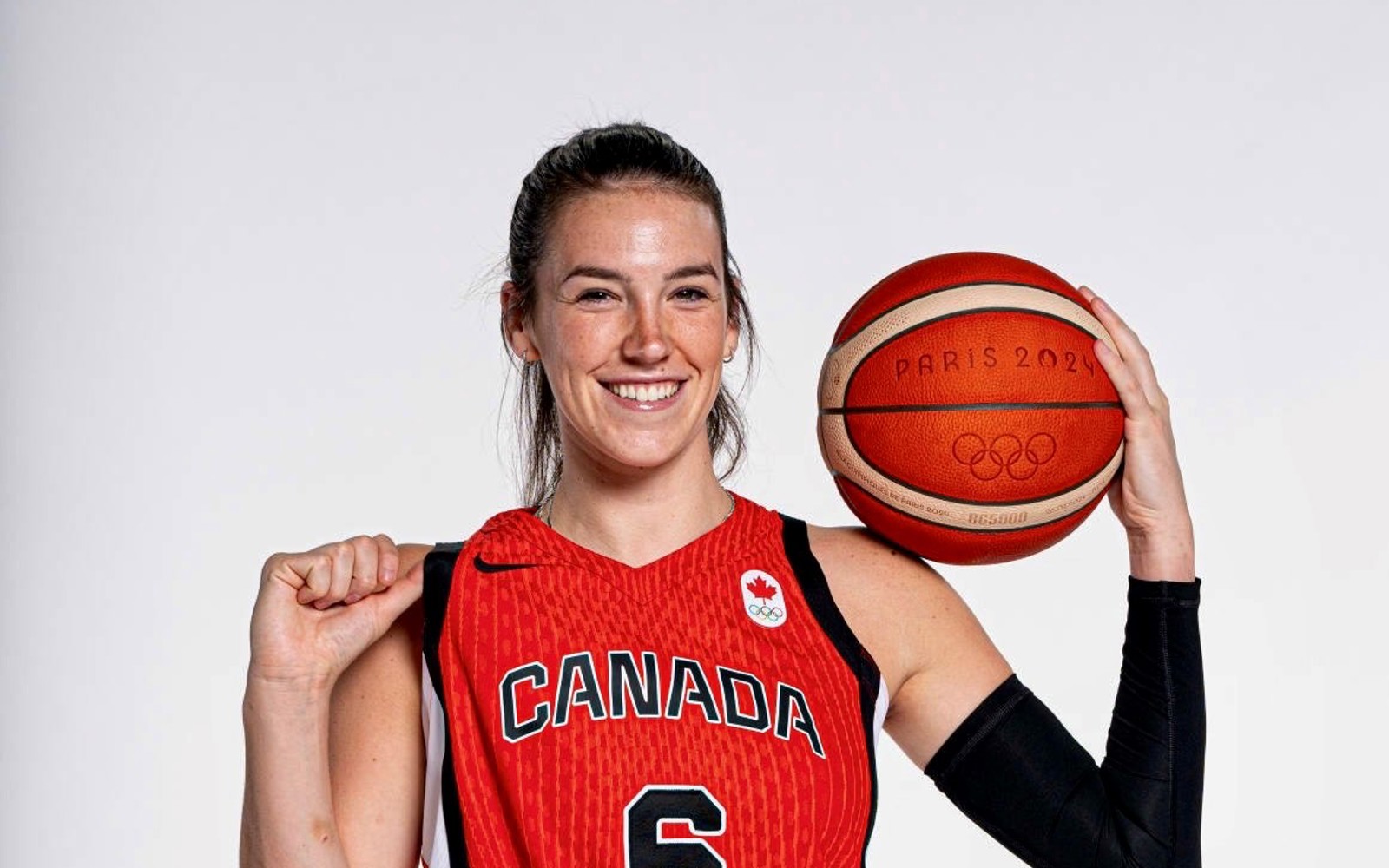 Woman in a red Team Canada basketball uniform holding a basketball that says Paris 2024