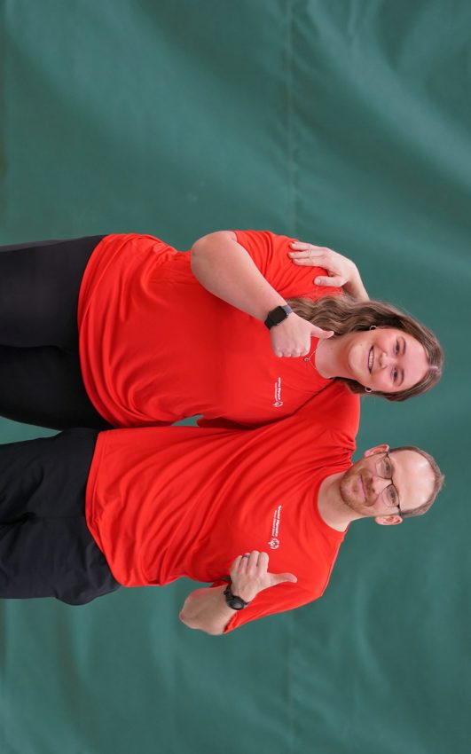 Two people in red shirts and black pants smiling at the camera