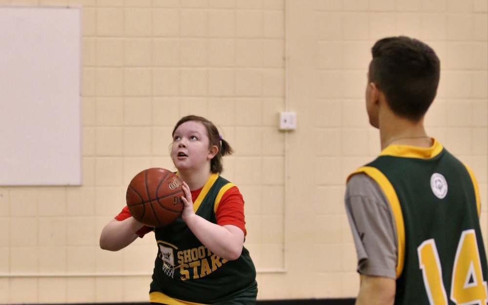 Two basketball athletes can be seen on the court. One athlete, you can only see their back. The other athlete is looking up and about to throw the ball in the hoop.