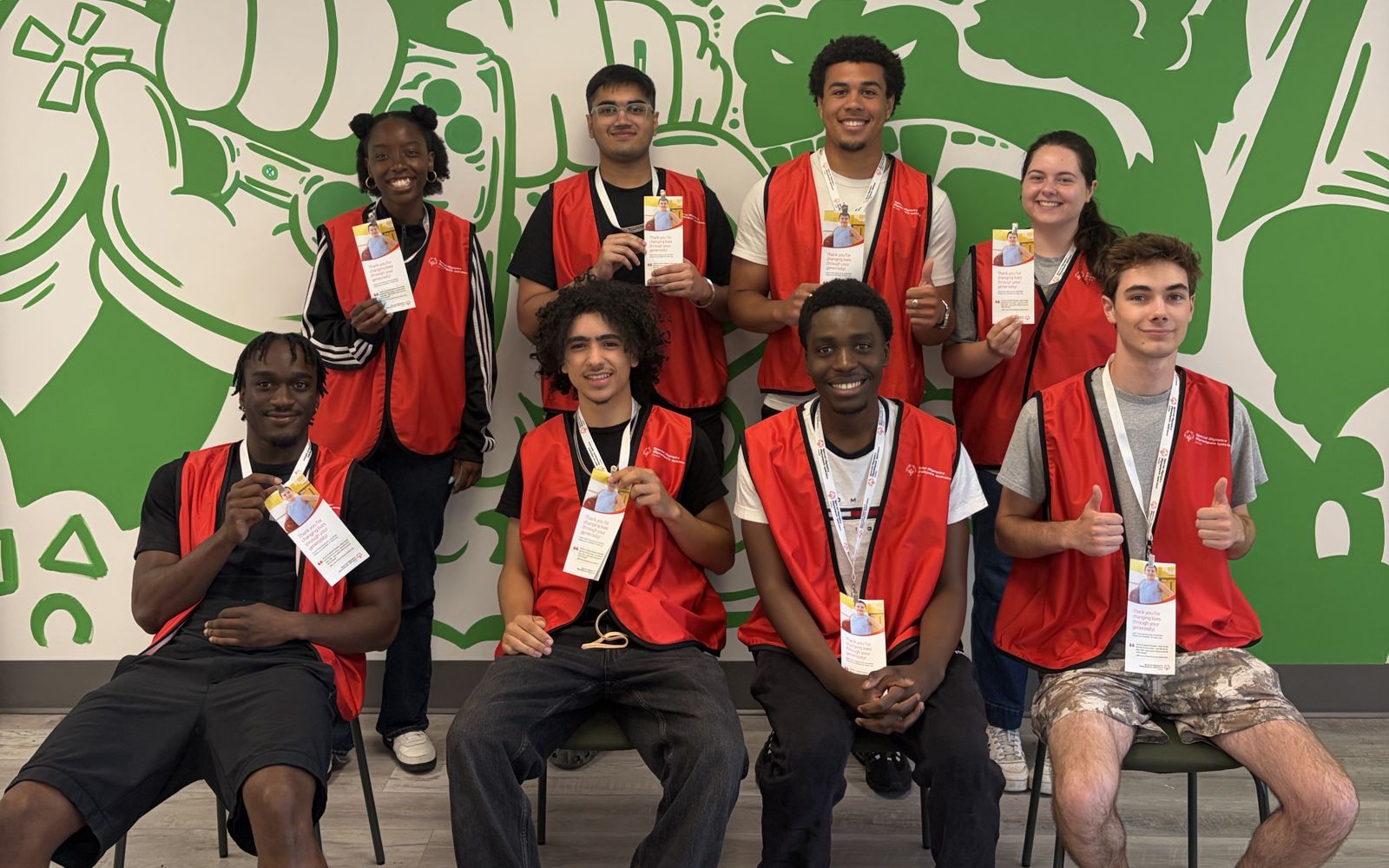 A group of 8 face to face canvassers pose together, smiling at the camera. The are all wearing red Special Olympics Canada branded vests. 