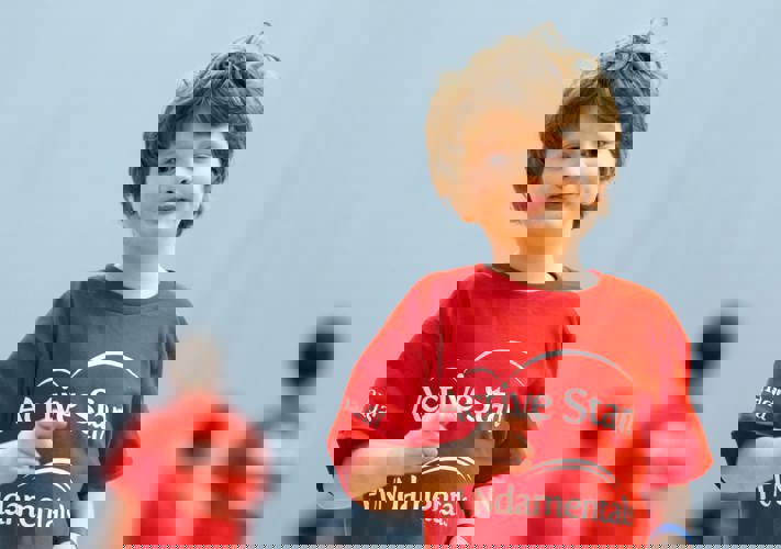 Young boy with brown hair and a red Active Start shirt running towards the camera.