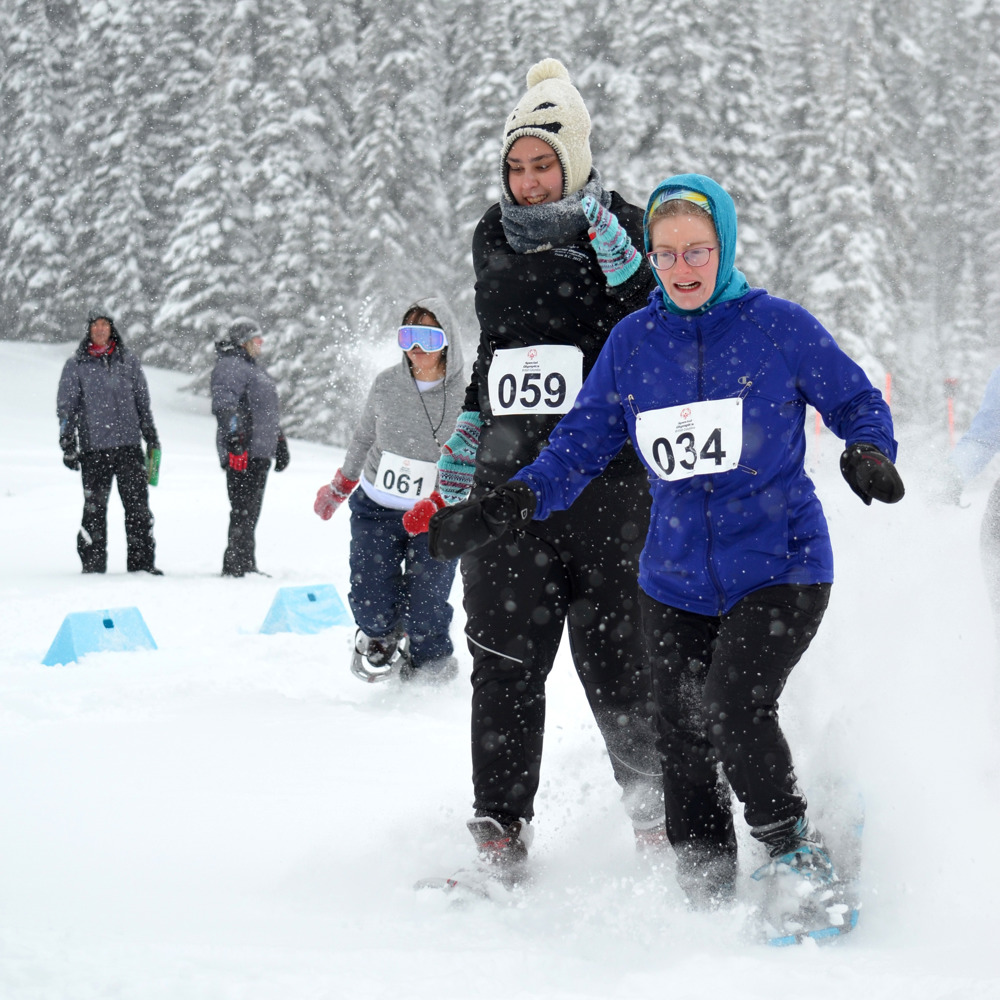 A pair of athletes with intellectual disabilities charge through the snow in their snowshoe race during the 2019 Special Olympics BC Provincial Winter Games.