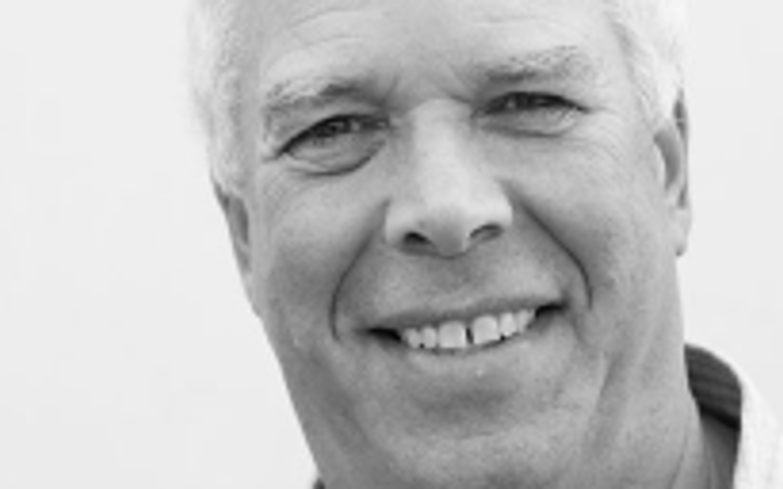 Photo en noir et blanc d'un homme souriant à l'appareil photo.