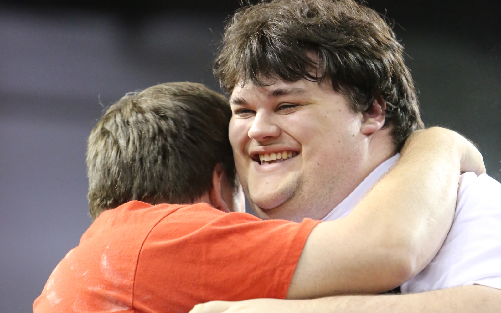 A powerlifting athlete smiles and is embraced by his coach after a good lift.
