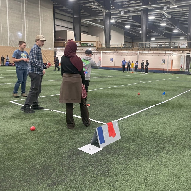 A unified sports match. Wide shot image of athletes playing bocce on a field. Four athletes are seen playing closer to the camera, while another group of athletes can be seen playing in the distance.