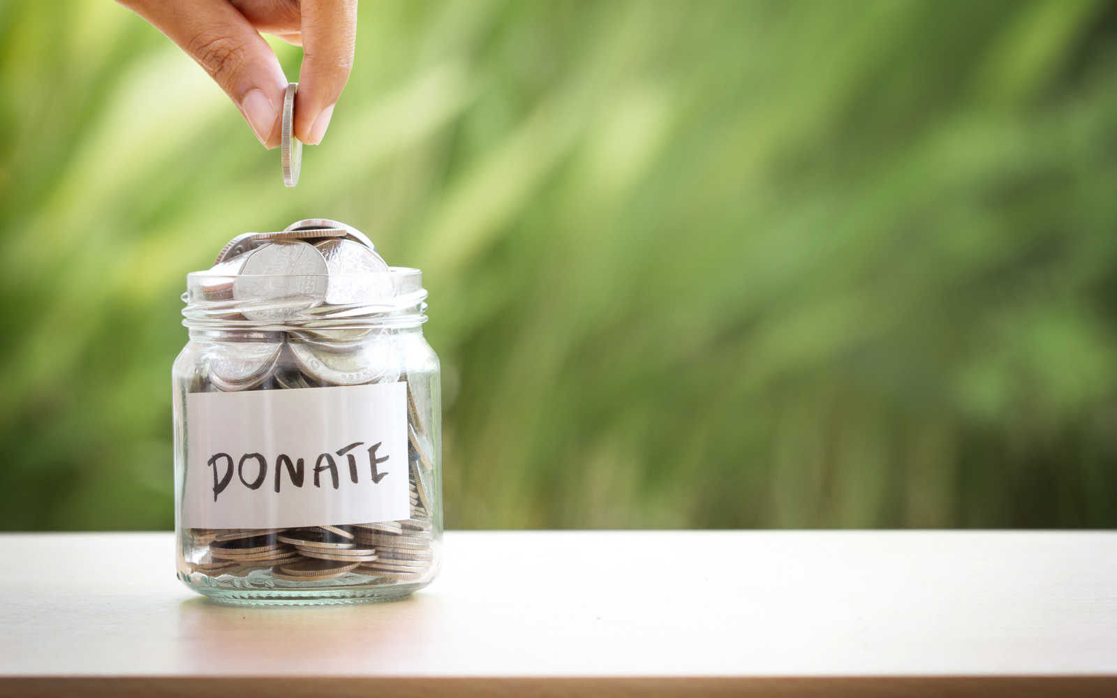 Hand putting money in a jar. Jar says donate on it. 