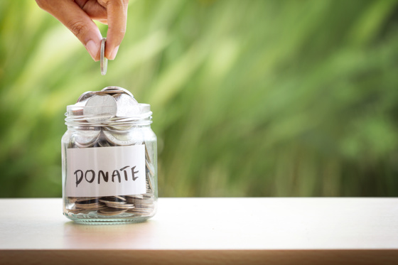Hand putting money in a jar. Jar says donate on it. 