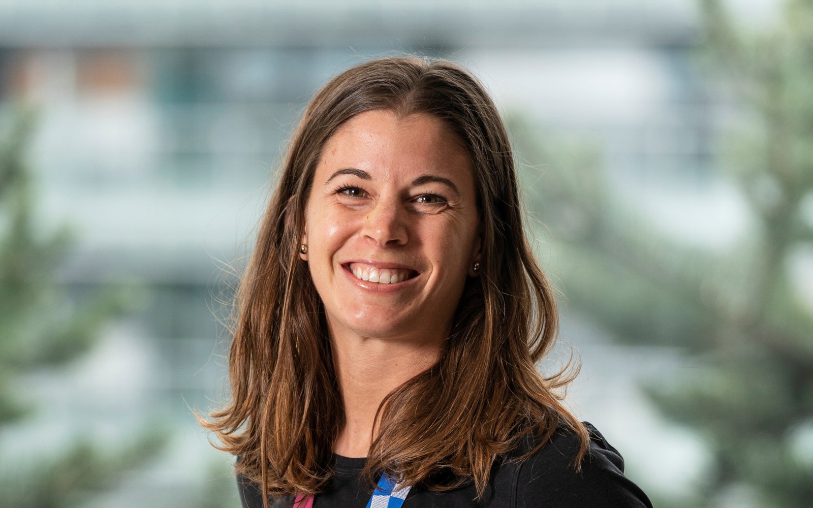 Headshot of a woman with long dark hair wearing a black shirt. Around her neck is an Olympic medal from Tokyo 2020.