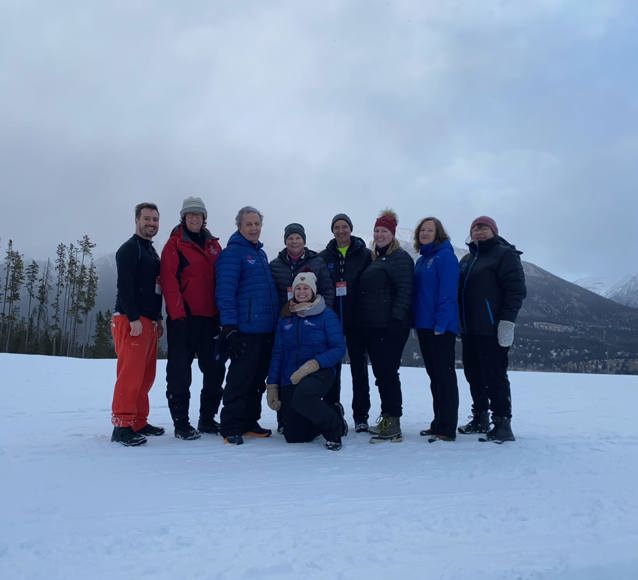 A group photo of everyone who was at the training camp. The photo takes place outside during the wintertime. Everyone is wearing winter jackets and smiling for the camera.