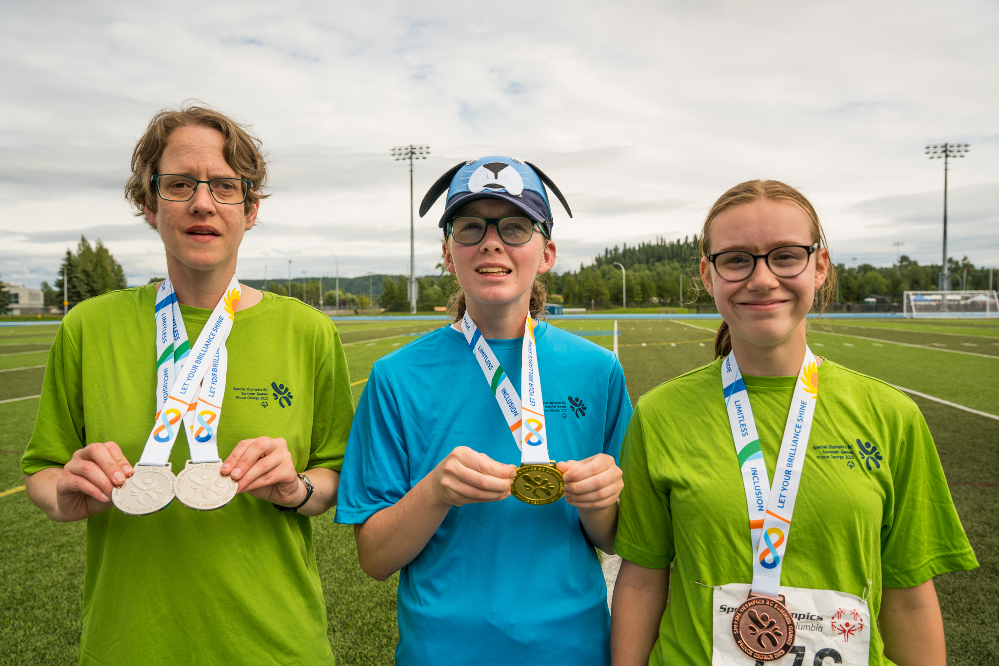 Three smiling athletes holding up their medals on a cloudy day