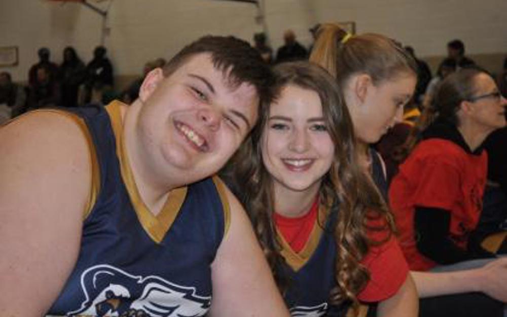 Two athletes smiling for the camera. They are wearing black and gold basketball jerseys.