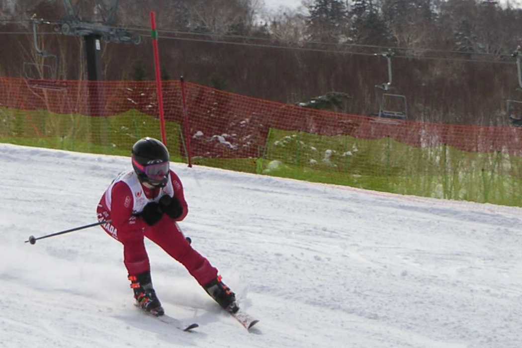 An athlete skiing down a slope. They are wearing a red skiing outfit with a black helmet and skis.