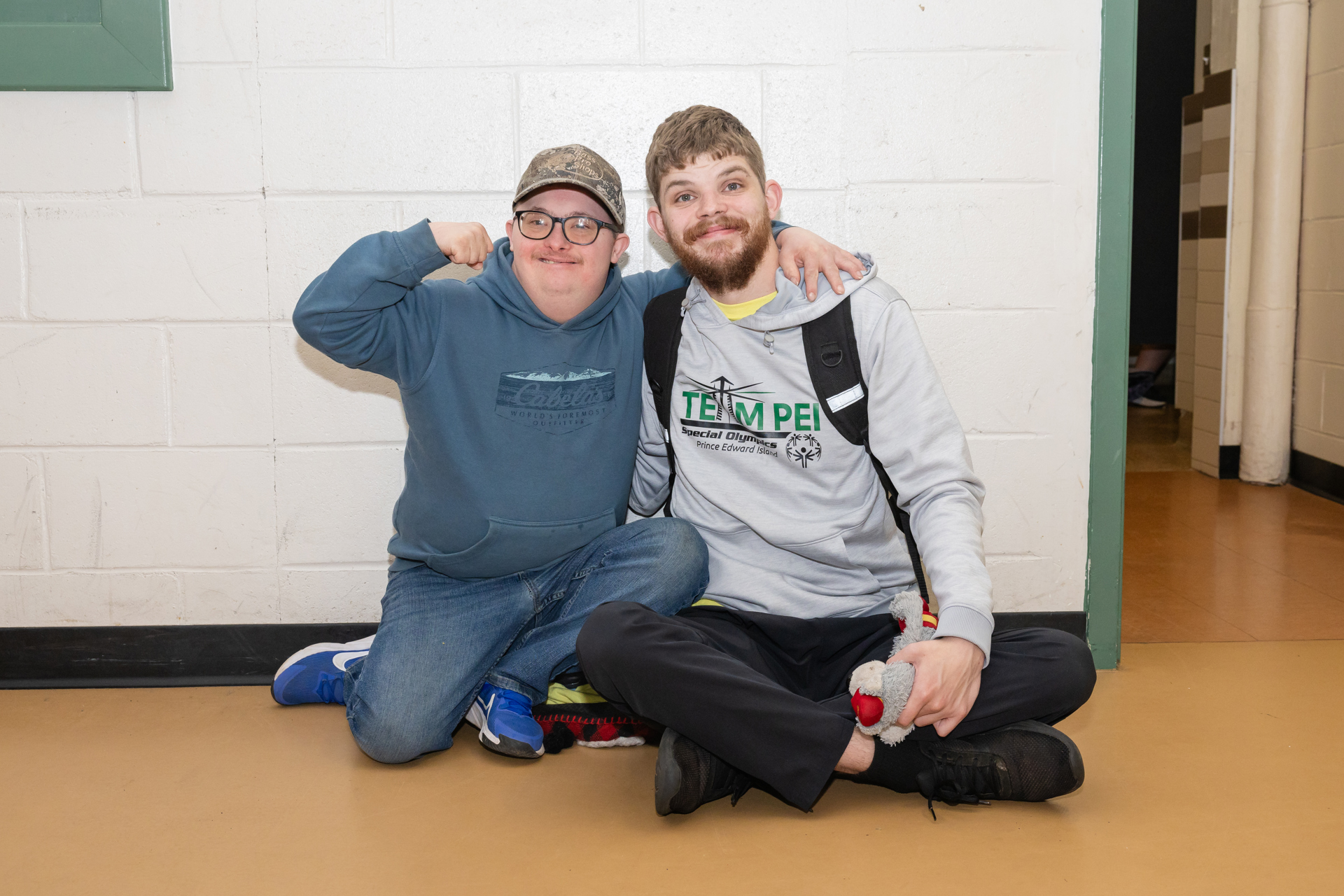 Two Special Olympics athletes sitting by a wall, smiling 