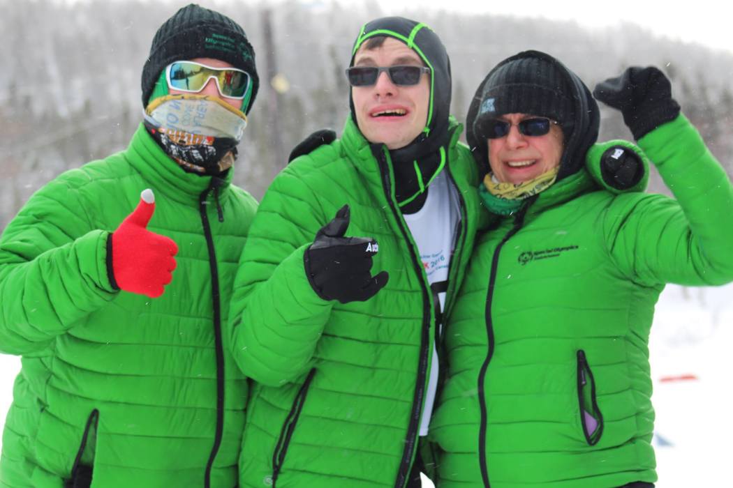 Three teammates in green Special Olympics Saskatchewan puffer jackets are smiling and giving a thumbs up to the camera.