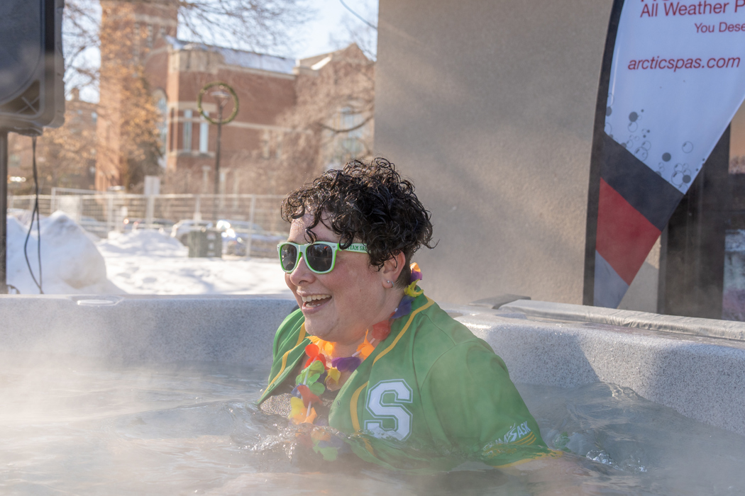 A individual taking a plunge in an ice cold water tub. She is wearing a green Saskatchewan baseball jersey and green sunglasses.