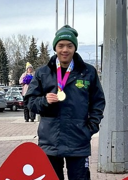 A photo of Michael, a Special Olympic Saskatchewan athlete. He is standing outside and wearing a winter jacket and toque. Around his neck is a medal and he is holding the medal with one hand. He is also smiling for the camera. A photo of Michael, a Special Olympic Saskatchewan athlete. He is standing outside and wearing a winter jacket and toque. Around his neck is a medal and he is holding the medal with one hand. He is also smiling for the camera.
