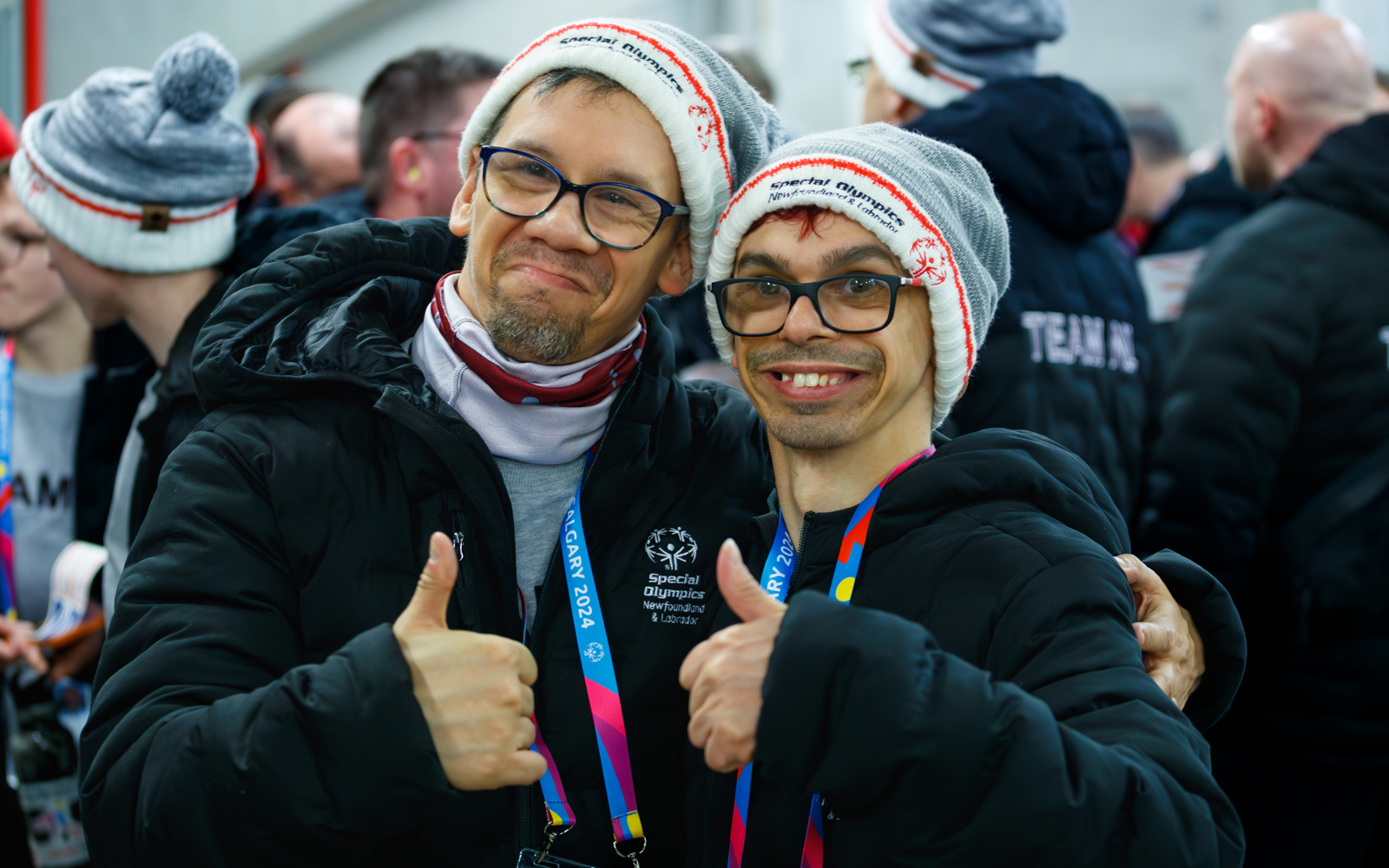 Two young men, both with glasses and a grey and white toque smiling at the camera and giving a thumbs up.