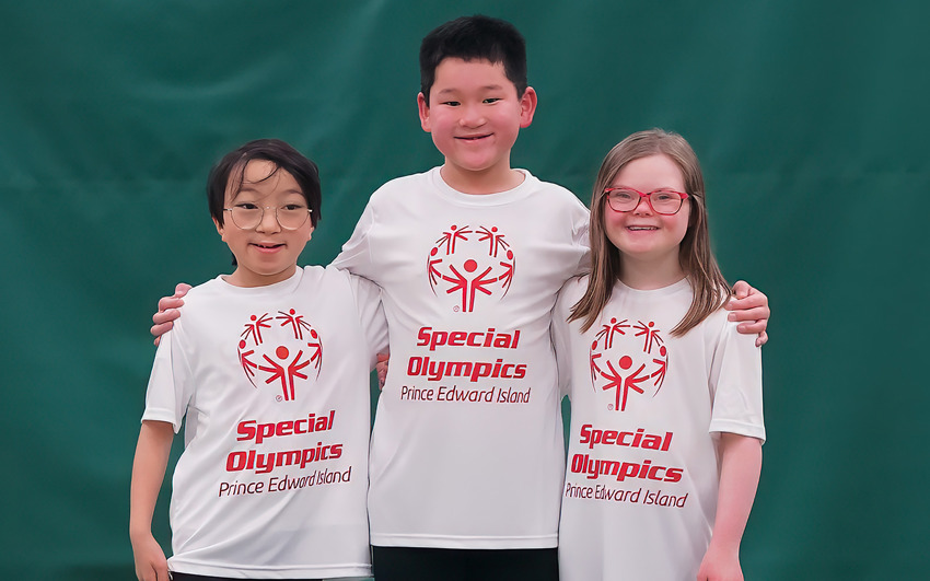 Three young kids stand in a line. All wearing Special Olympics white shirts and black pants. 