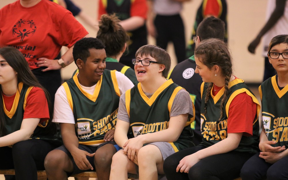 Three basketball athletes sitting on the bench. They are all talking with each other and smiling and laughing.
