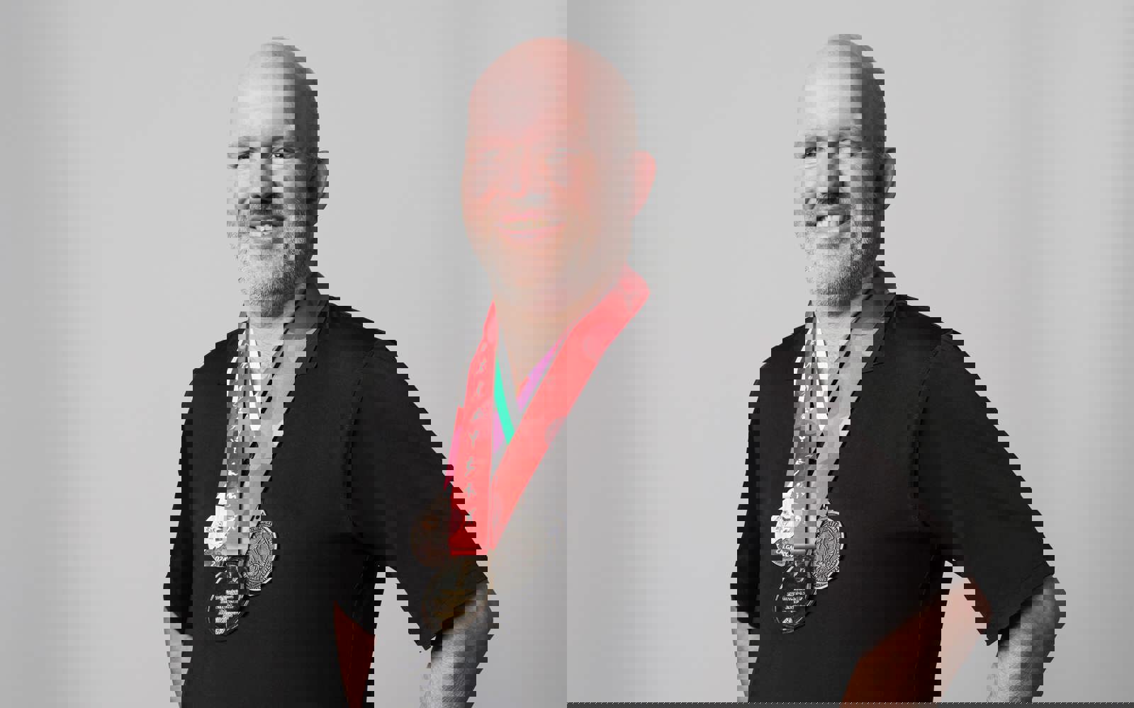 Older man in all black wearing medals around his neck. 