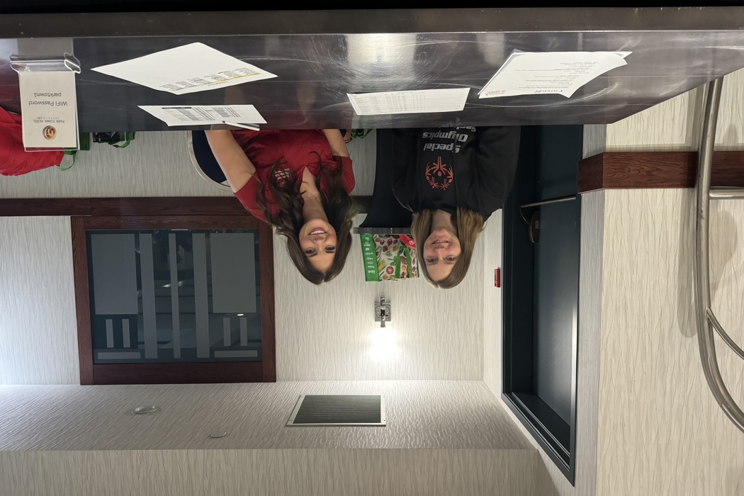 Two volunteers are sitting behind a table and smiling for the camera. In front of them are stacks of paper.