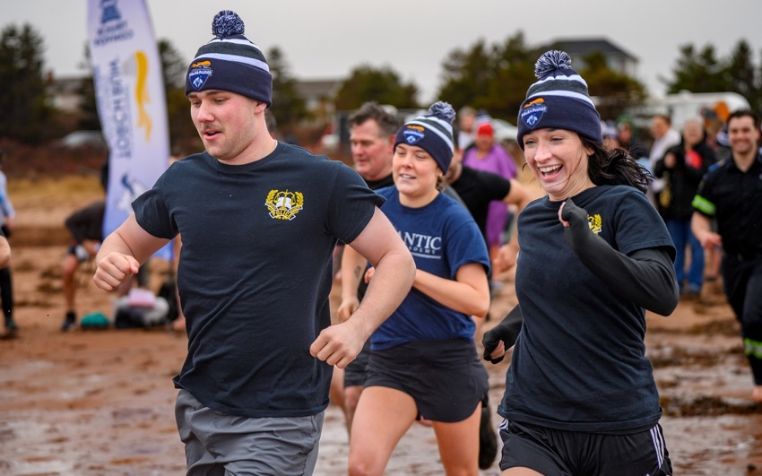 A group of people run into the water on the beach for a Polar Plunge event