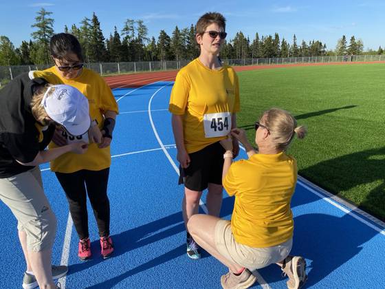 Two athletes in yellow shirts having competition bibs pinned on them by volunteers on a race track. 