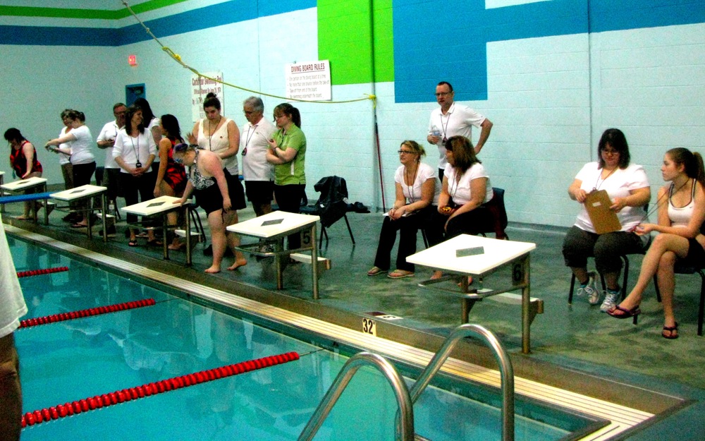 Multiple volunteers in white t-shirts are sitting next to a swimming pool preparing for a match.