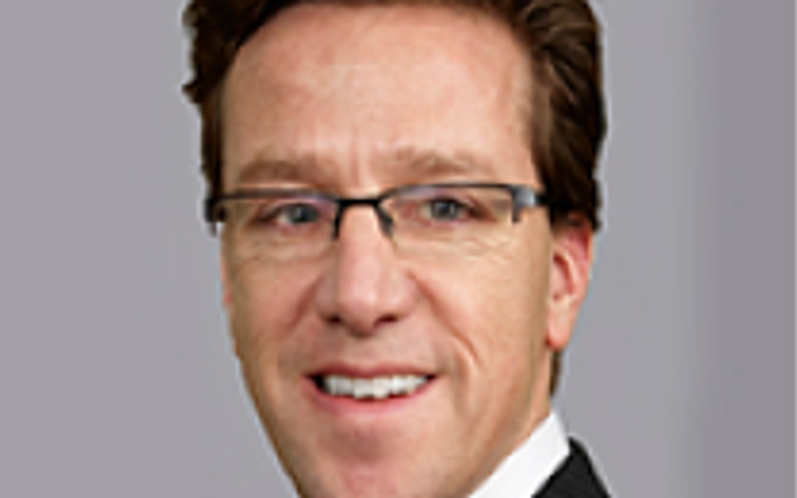 Homme en costume noir, chemise blanche et cheveux noirs, souriant à l'appareil photo.