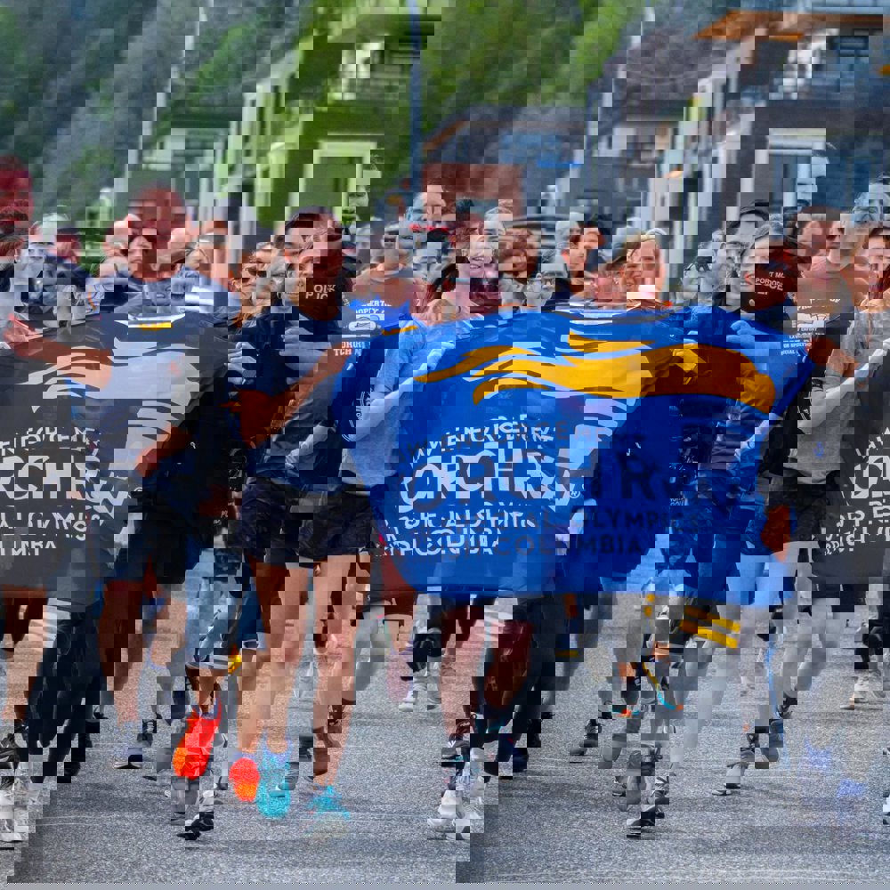 A group of participants run together holding a banner at the Port Moody Police Department Law Enforcement Torch Run Torch Run event.