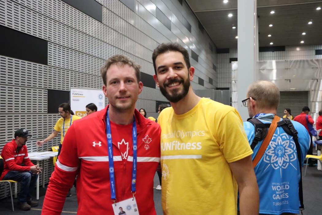 Two men standing beside each other staring into the camera. One is in Special Olypmics Team Canada gear, the other is in a yelow FUNFitness t-shirt. 