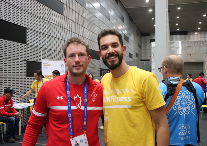 Two men standing beside each other staring into the camera. One is in Special Olypmics Team Canada gear, the other is in a yelow FUNFitness t-shirt.