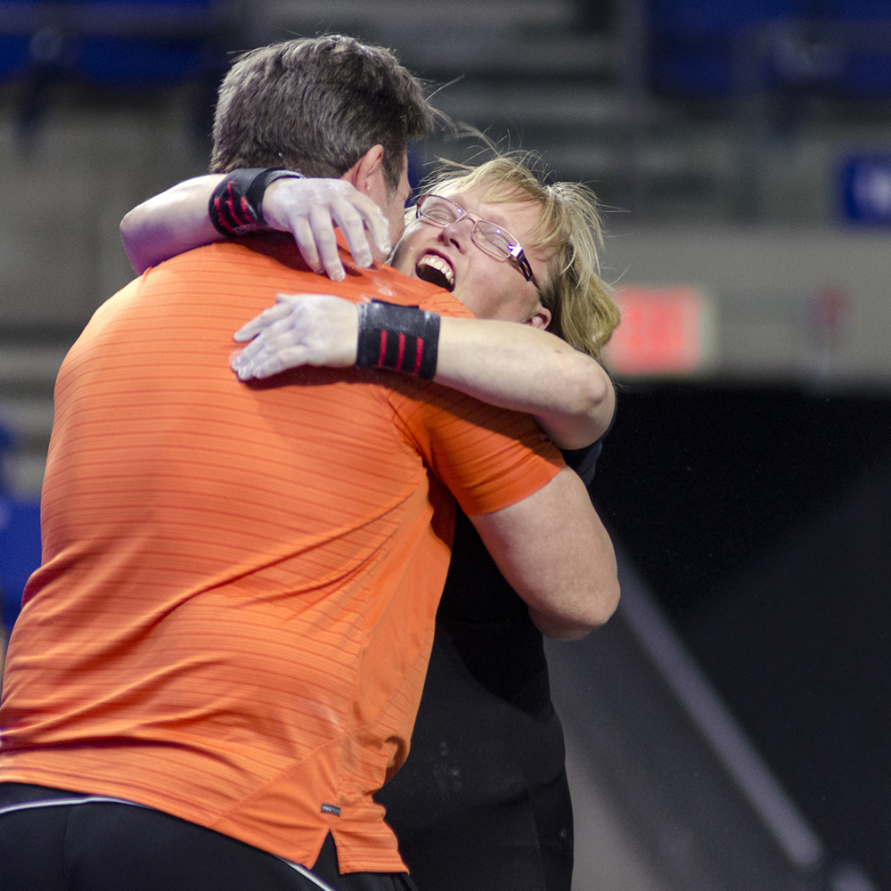 A coach and powerlifting athlete embrace at a competition.
