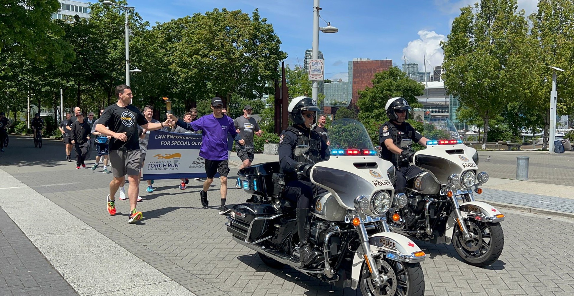 Participants run behind a police escort by two motorcycle officers while carrying the Law Enforcement Torch Run flame.