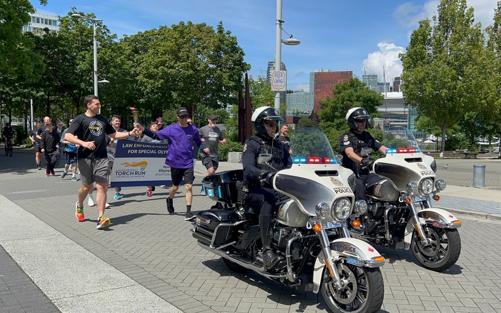 Participants run behind a police escort by two motorcycle officers while carrying the Law Enforcement Torch Run flame.