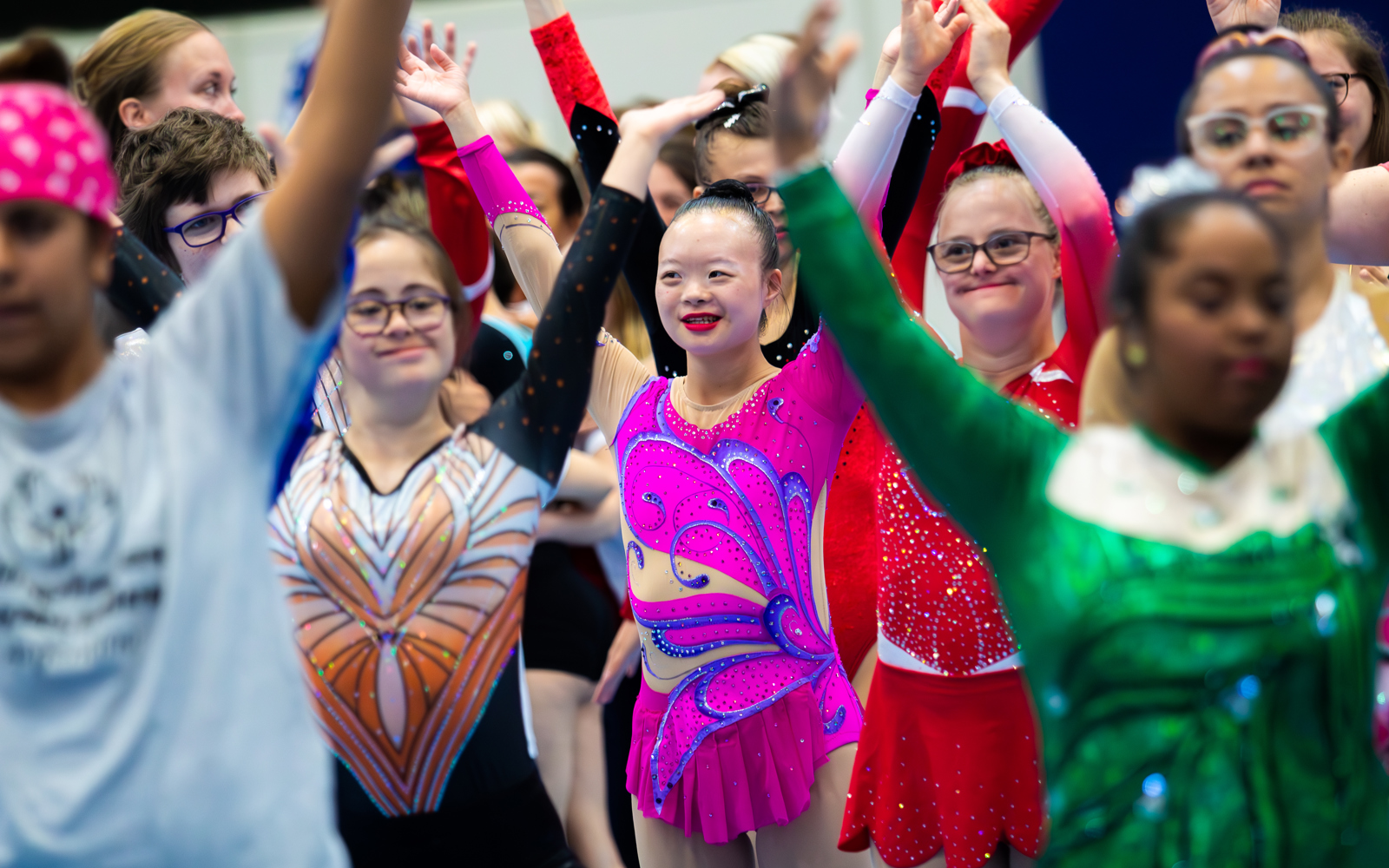 Group of athletes with arms in the air. All are smiling and wearing figure skating costumes 