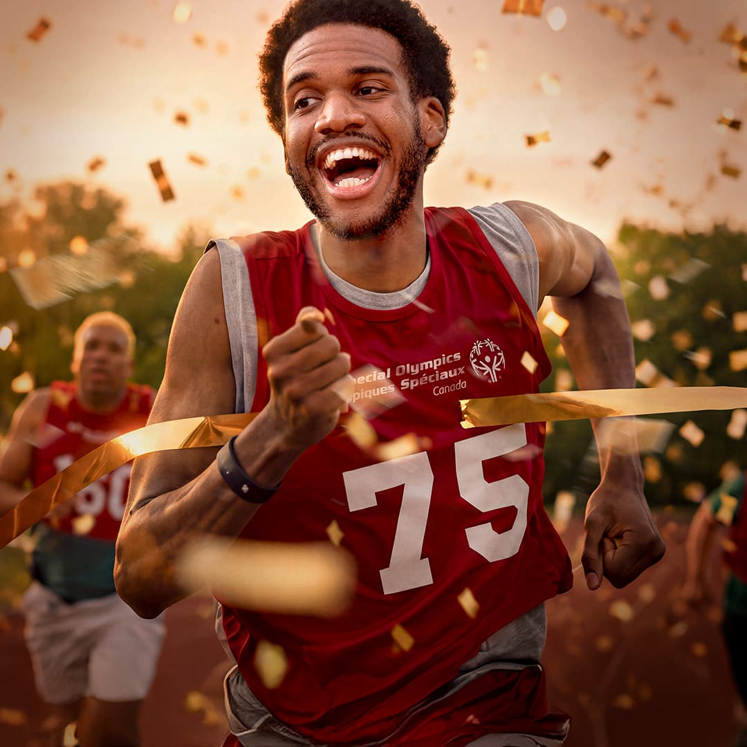 Man in a red special olympics shirt running while gold confetti falls around him Man in a red special olympics shirt running while gold confetti falls around him