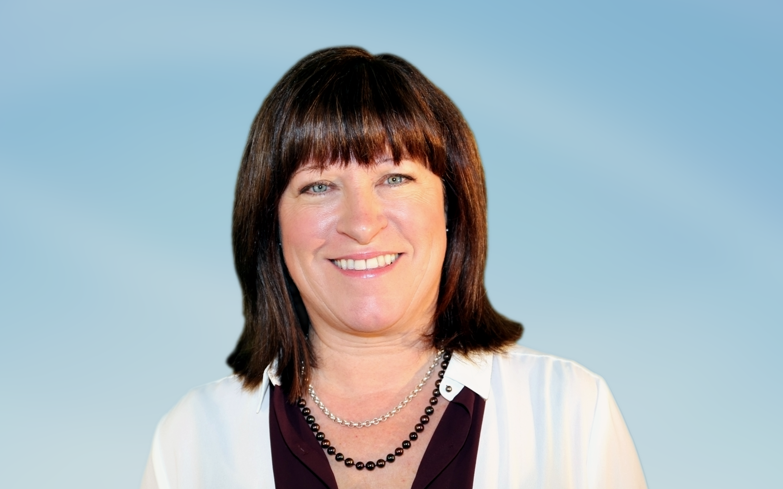 Woman with black blouse and white blazer. She is wearing two necklaces - a black beaded and a silver chain. She is smiling at the camera.