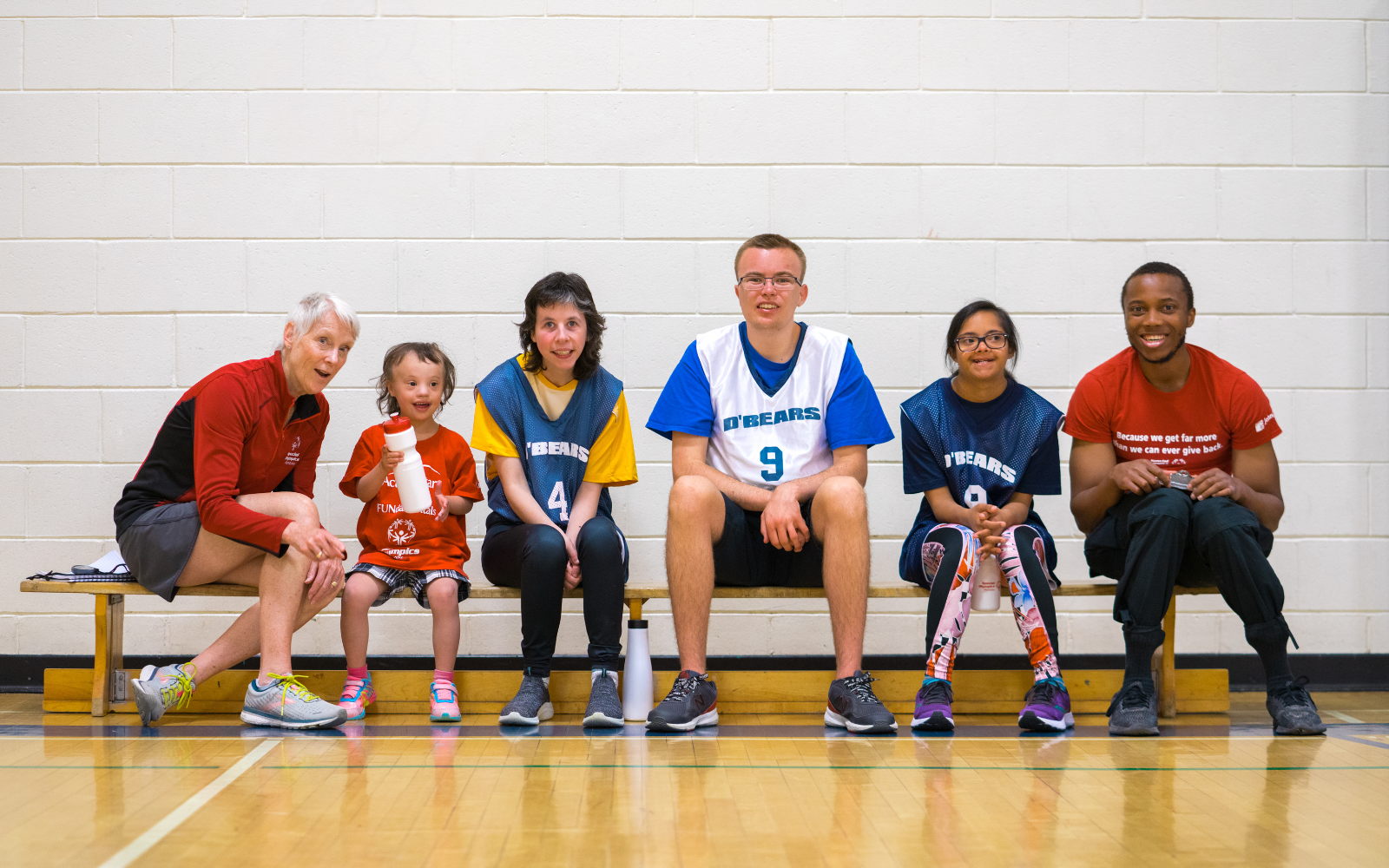 Diverse group of people sitting on a bench smiling at the camera.