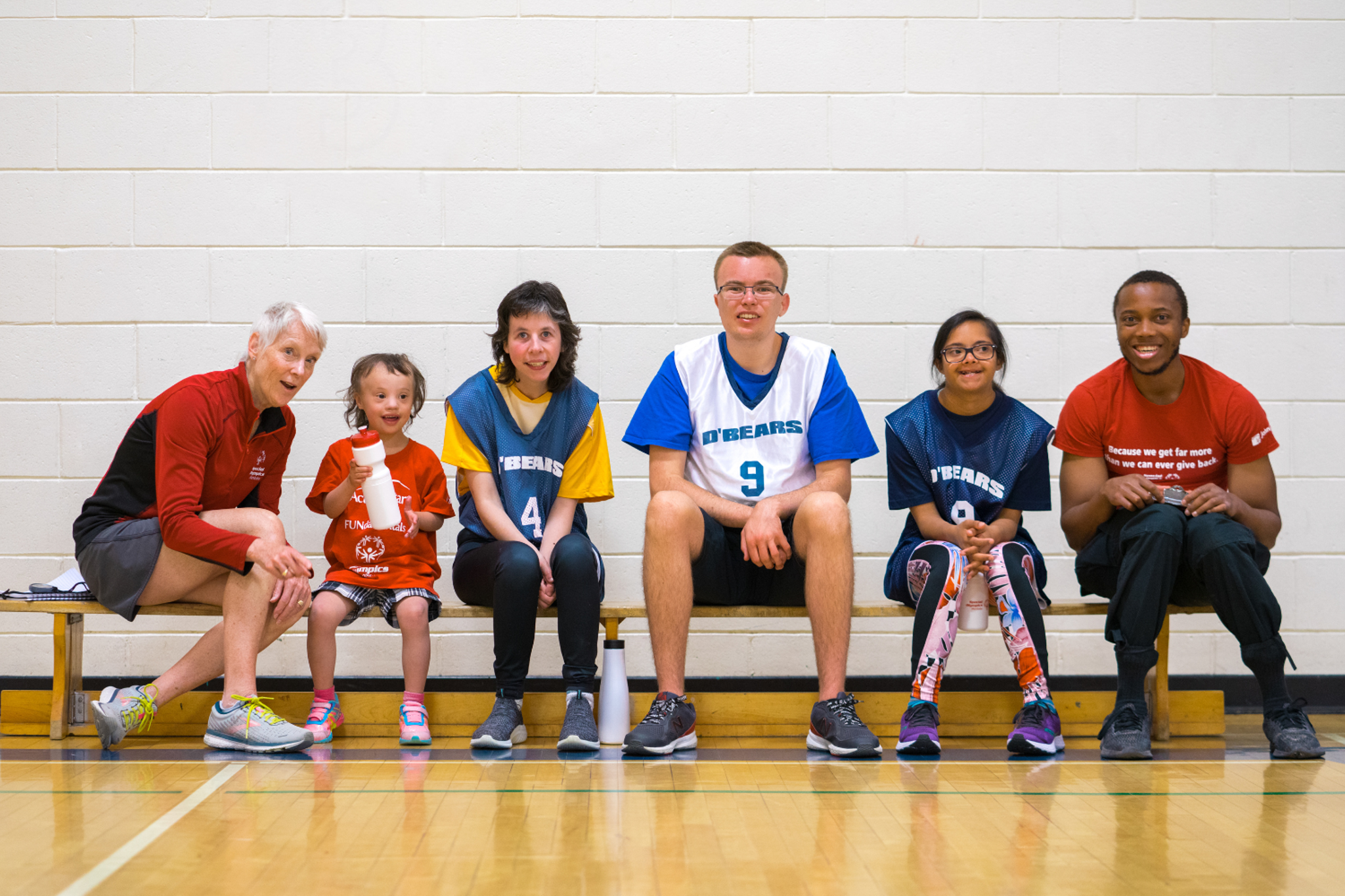 Diverse group of people sitting on a bench smiling at the camera.