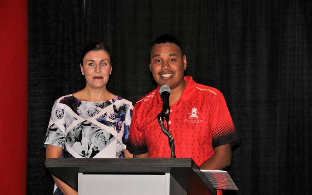 Two individuals are standing behind a podium and a microphone and giving a speech. They both look very happy to be giving their speech.