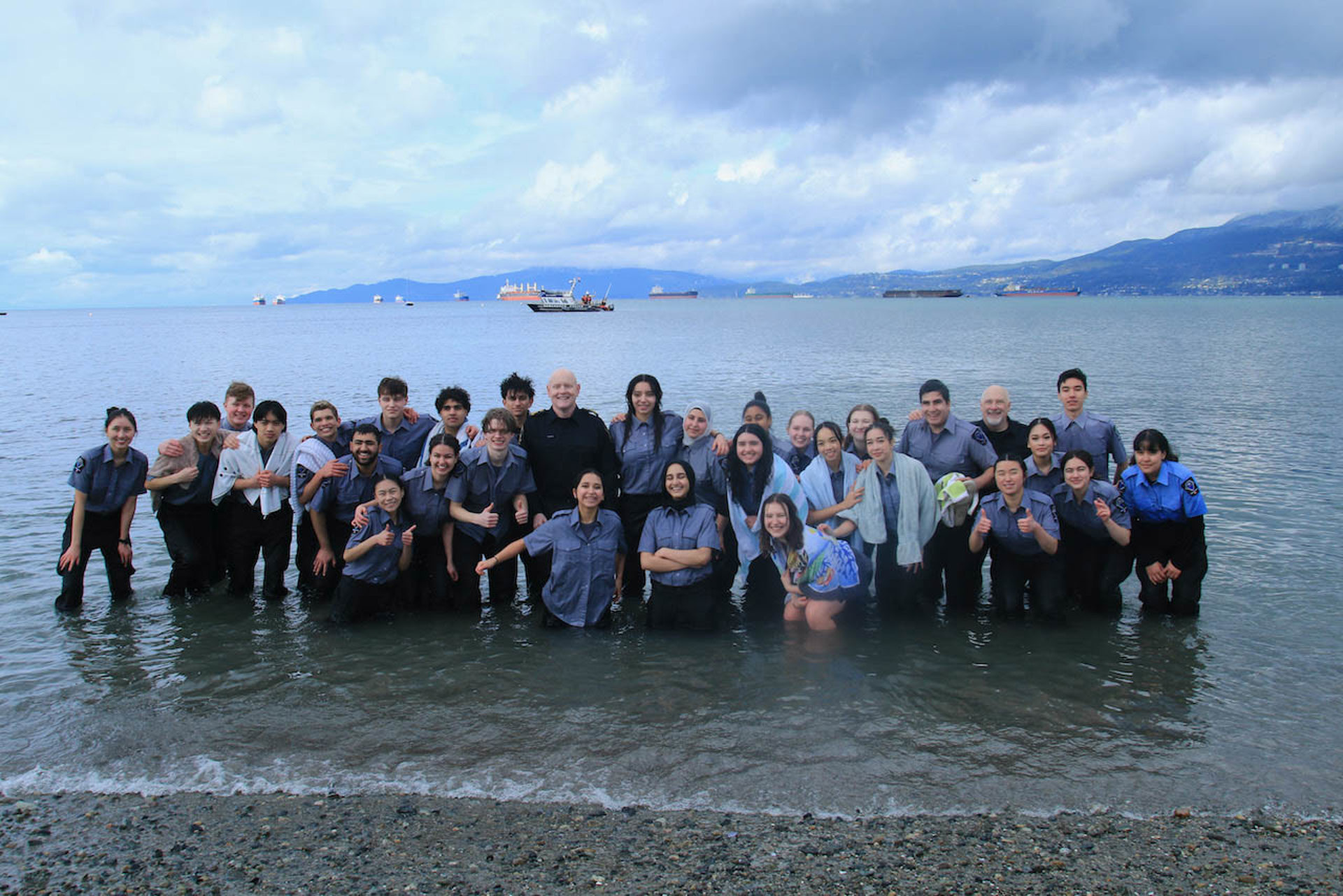 A large group of participants pose together in the shallow waters of English Bay looking proud.