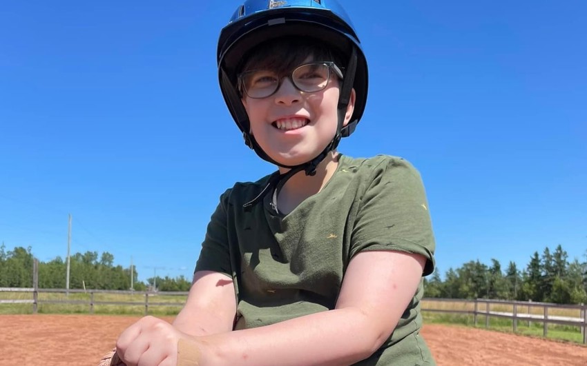 Gabe wearing a helmet while sitting on top of a horse outside. 