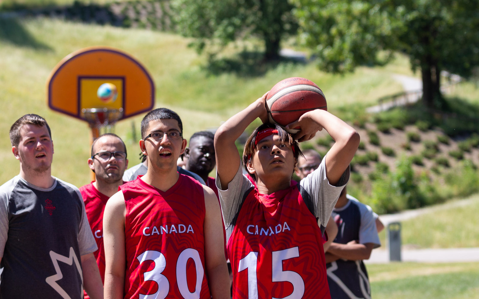 Diverse group of people on a basketball court. One boy is about to throw a basketball. 